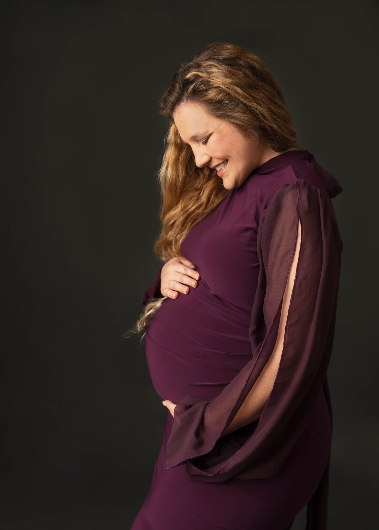 pregnant mom holding belly and smiling down wearing purple maternity gown taken by utah county photographer