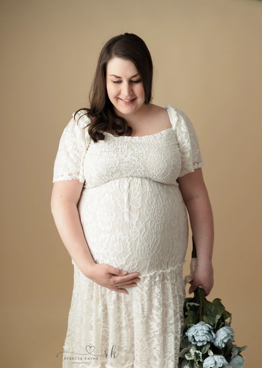 woman in white maternity gown holding a bouquet of blue flowers