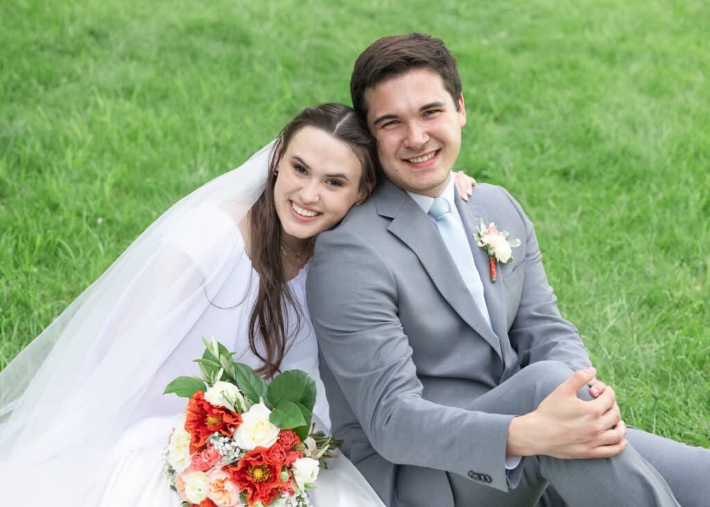 bride and groom sitting on grass smiling at camera