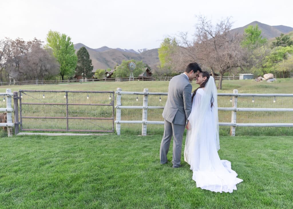 bride and groom in front of white fence on a farm