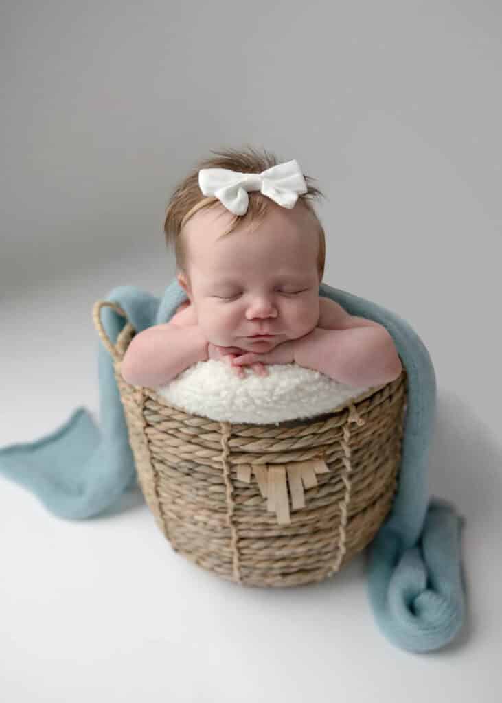 newborn baby wearing white bow with blue blanket in basket