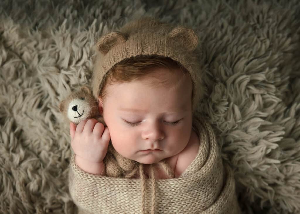 newborn baby in bear hat with teddy bear on brown blanket