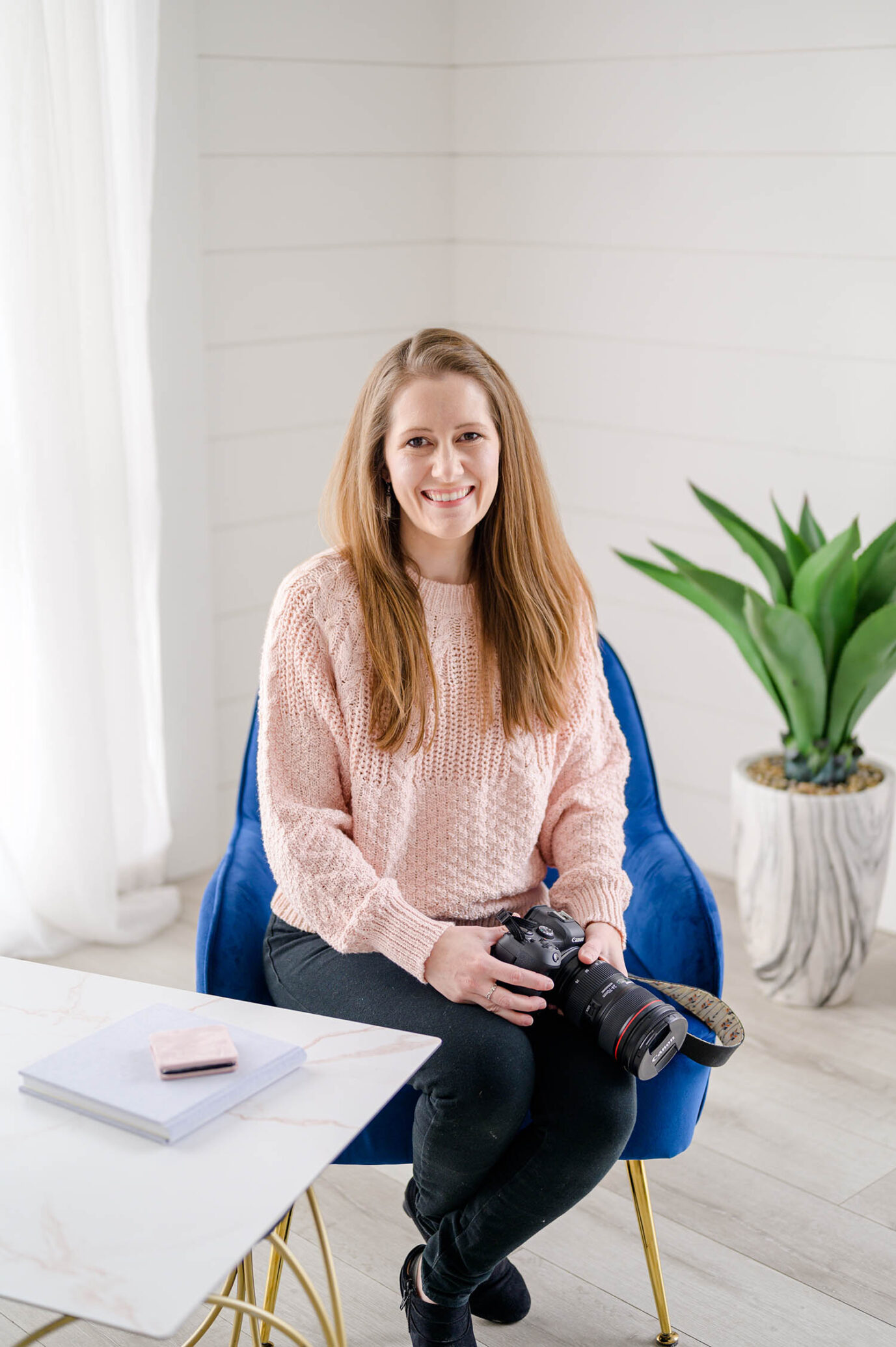 utah newborn photographer in a pink sweater holding her camera next to albums in utah county studio Utah newborn photography package