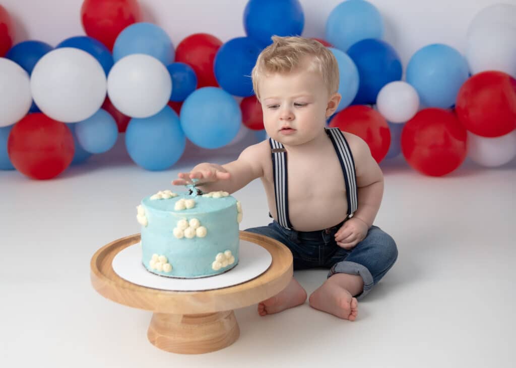 Baby cake smash session baby eating cake with clouds in front of balloon arch