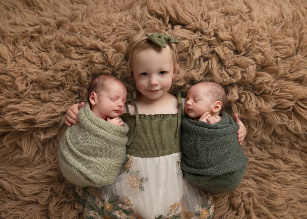 baby girl holding twin brothers in a utah twin newborn photography session